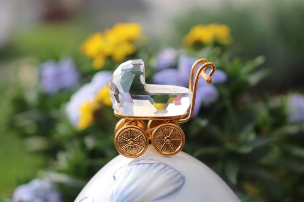 baby carriage, crystal figurine, gold decoration, new baby, baby shower, elegant gift, miniature pram, baby symbol, celebration, motherhood, birth announcement, decorative item, sparkling crystal, golden wheels, delicate ornament, baby theme, floral background, macro shot, close up, keepsake, luxury detail, gift idea, new life, parenting, baby celebration