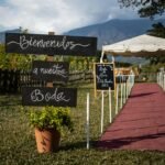 Outdoor wedding setup with welcome sign in Spanish and a red carpet path under clear skies.